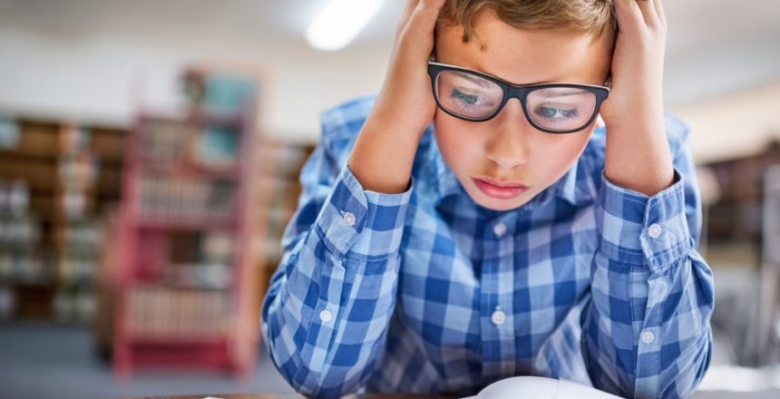 Featured image showing an elementary aged boy struggling over his text book in a library