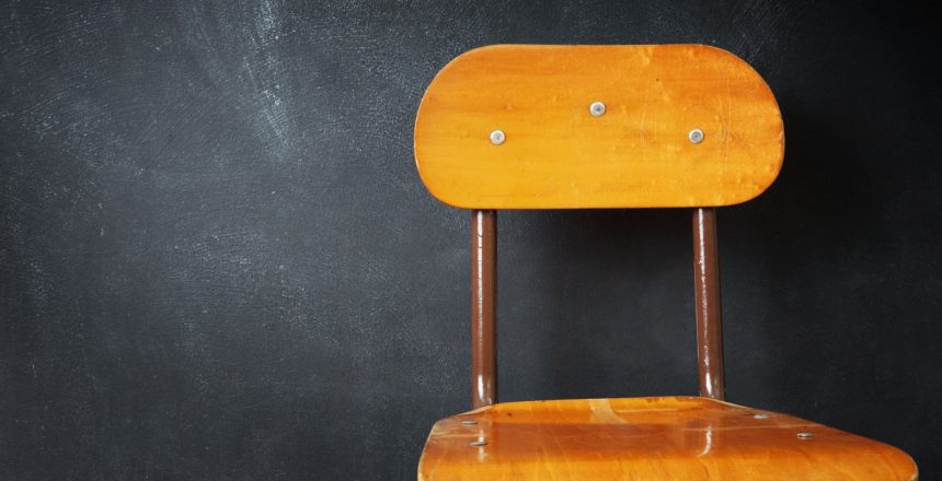 Featured image showing empty wooden school chair against a black chalkboard in school